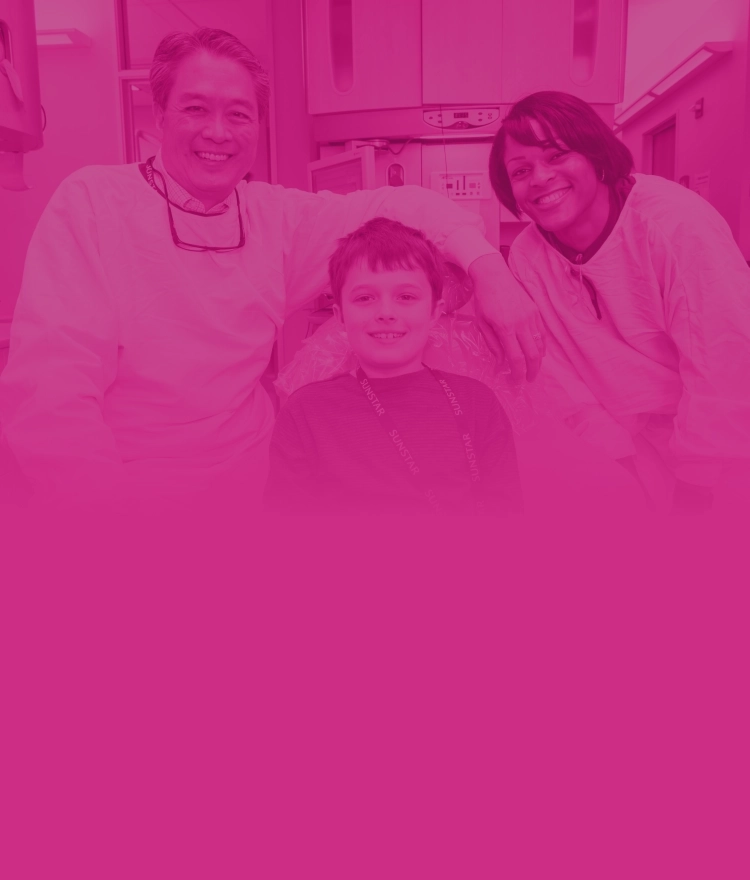 A young boy smile in an exam chair with a male and female provider on either side.