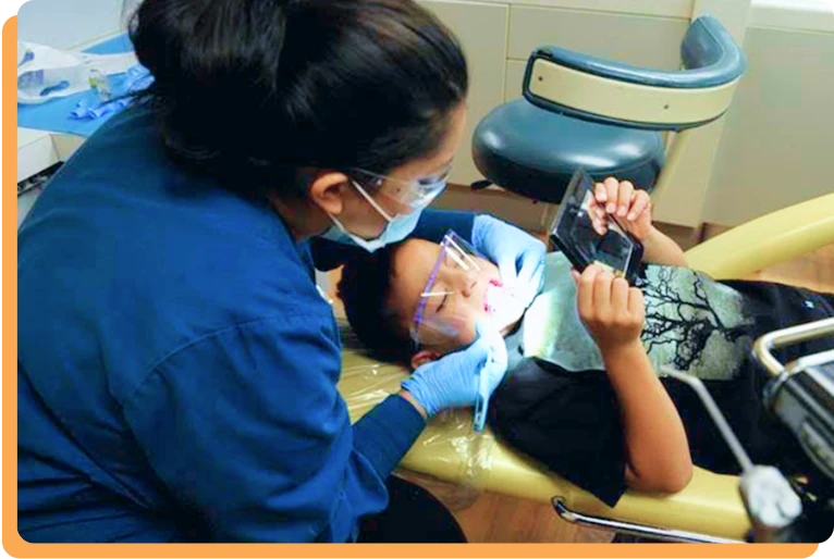 A pediatric dentist cleaning a patient’s teeth